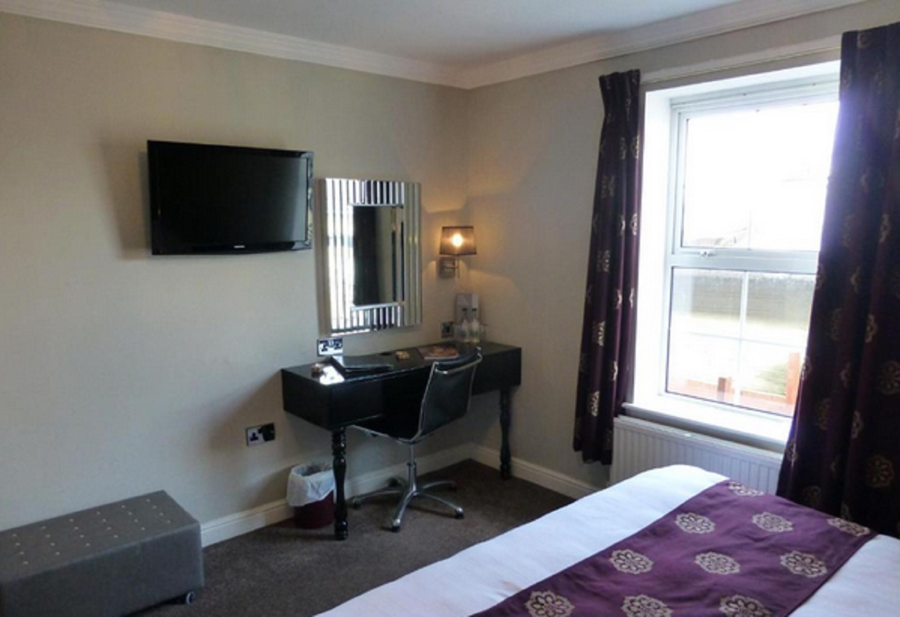 A hotel room with a bed, a desk, a chair, a television, a window with curtains, and a lamp.