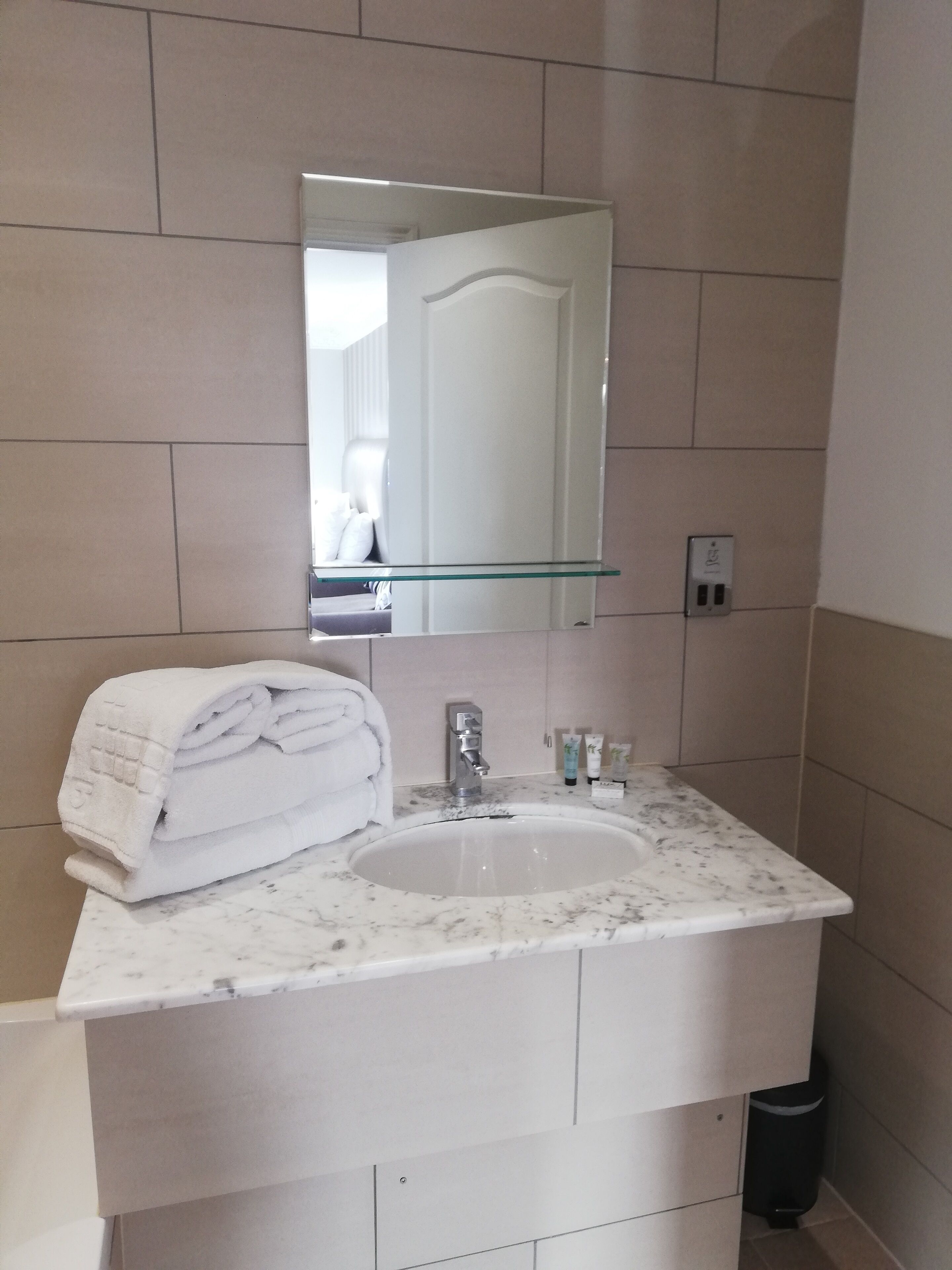 A bathroom with a white marble sink, a glass shelf above the sink, and a mirror.