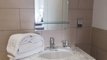 A bathroom with a white marble sink, a glass shelf above the sink, and a mirror.