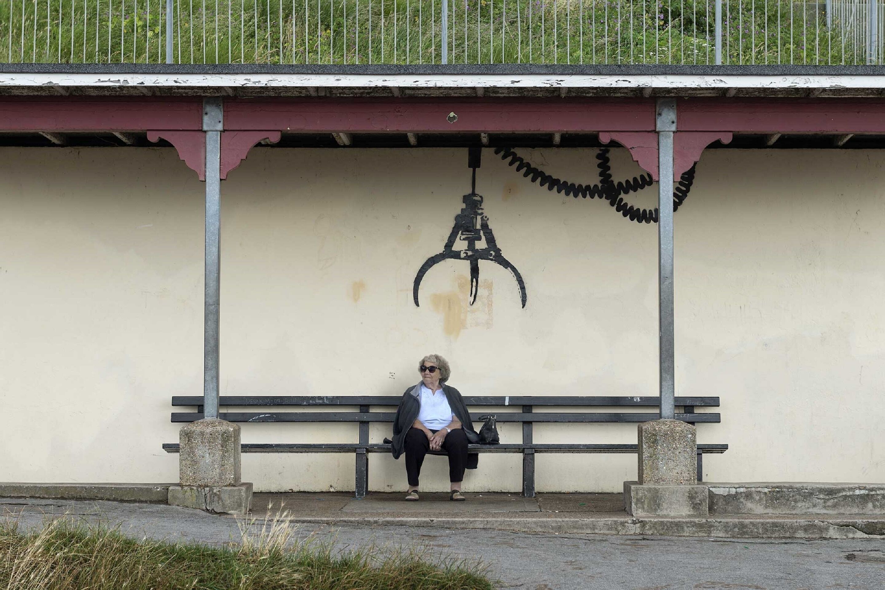 A bench under a shelter with a simple, unadorned wall and a metal railing.