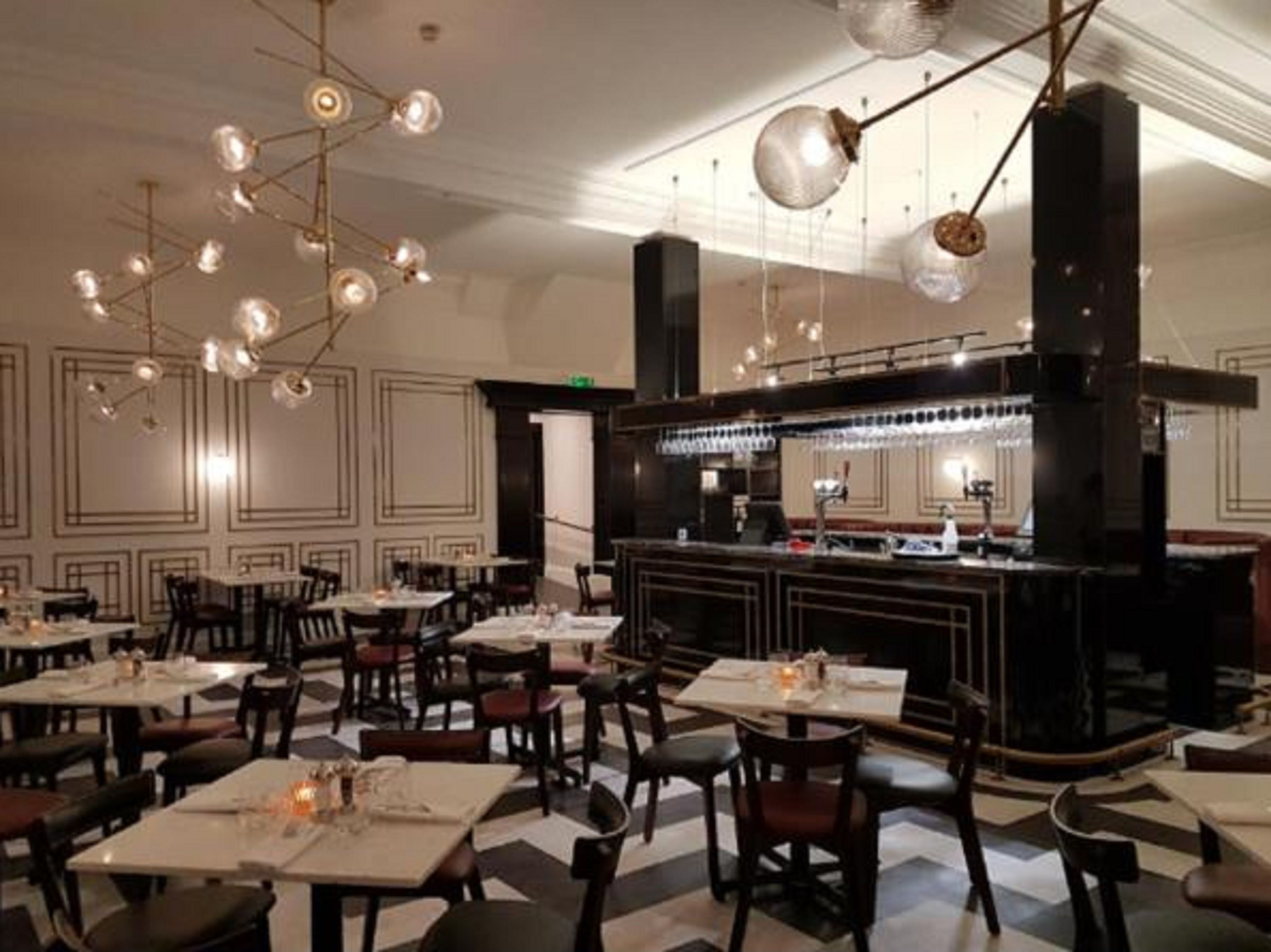 Ein Restaurantinneres mit Tischen, Stühlen, einer Bar und einem modernen Kronleuchter.