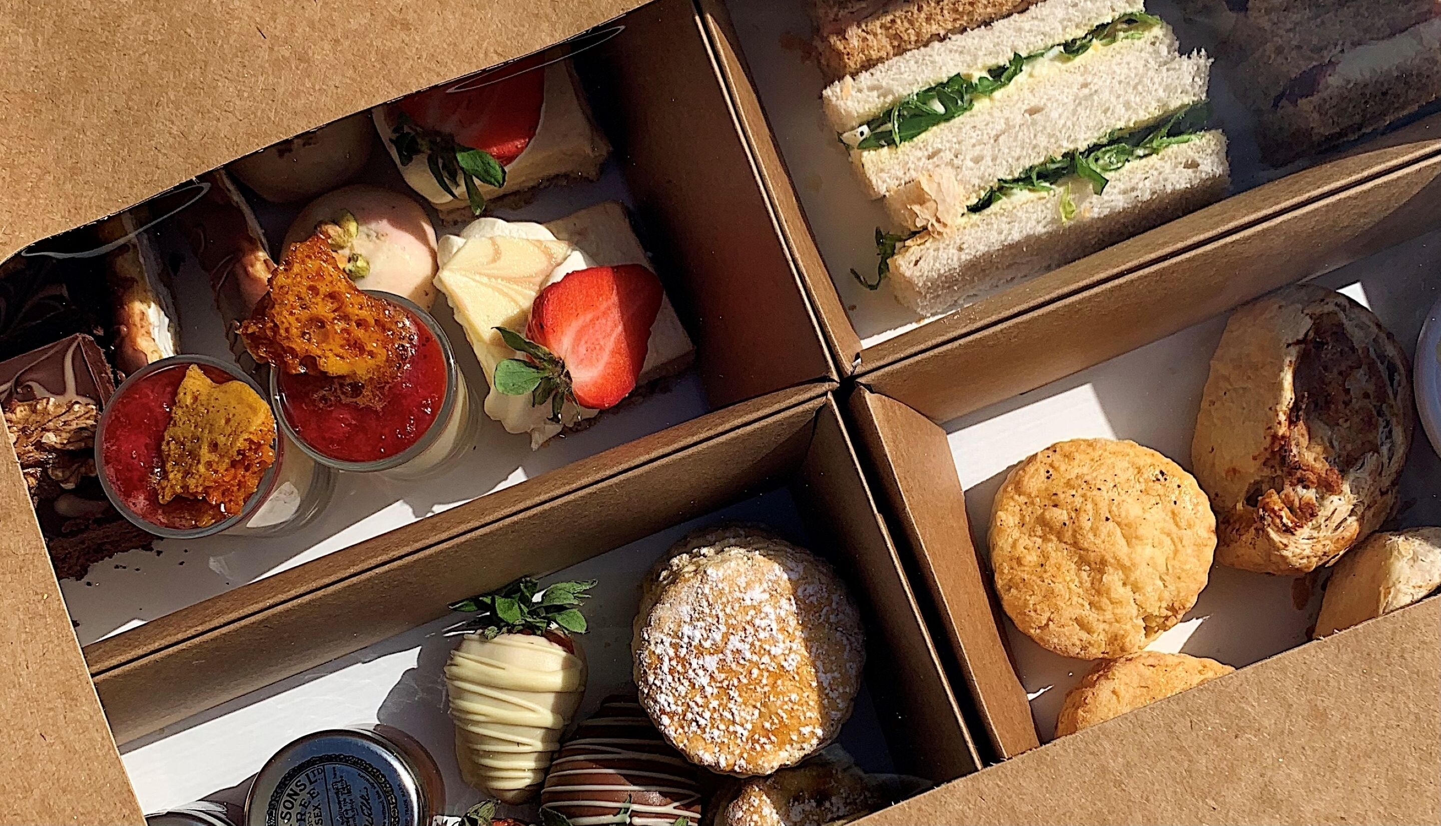 A variety of food items including sandwiches, pastries, and desserts in a cardboard box.