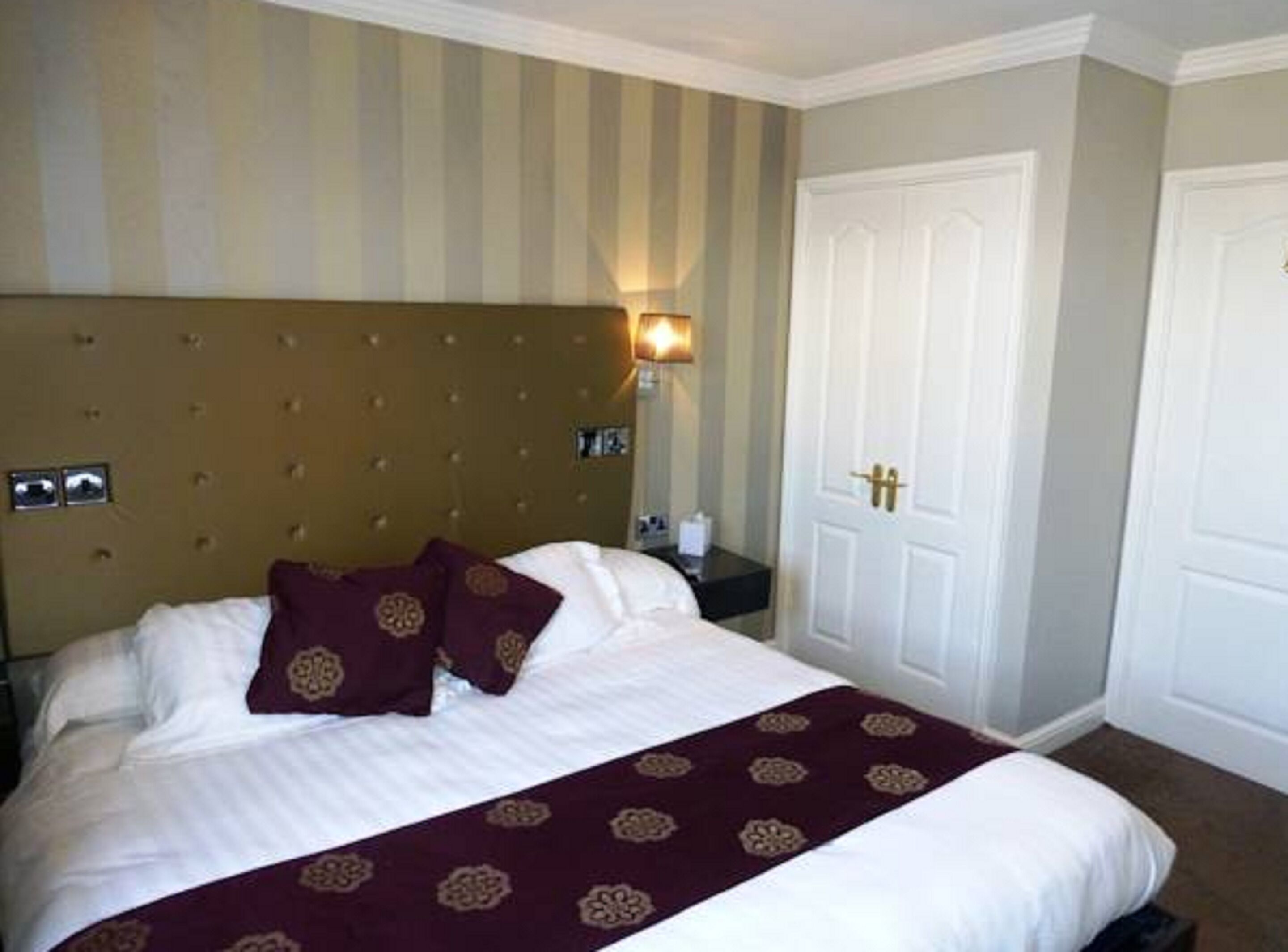 A hotel room with a large bed, striped wallpaper, a tufted headboard, and a white door.