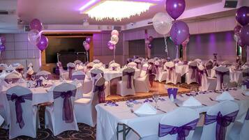 A banquet hall with round tables, white tablecloths, and purple sashes on chairs.