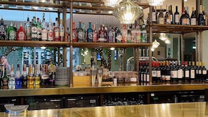 Un espace bar avec des étagères remplies de différentes bouteilles d’alcool, un comptoir et des luminaires en cristal suspendus.