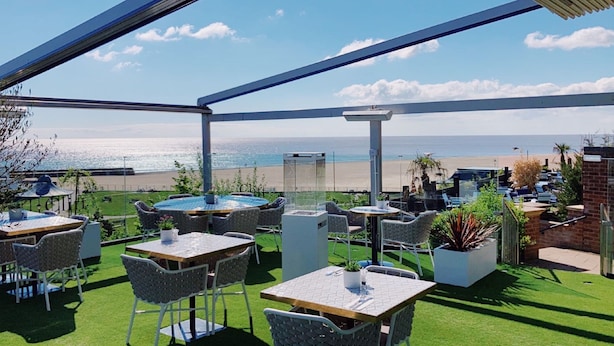 Une terrasse extérieure avec des tables et des chaises, un jacuzzi et une vue sur la plage.