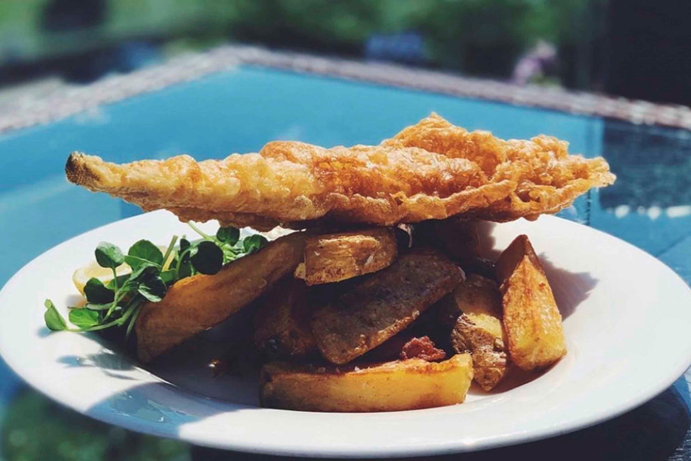 Une assiette de poisson frit et de pommes de terre, servie au bord d’une piscine.