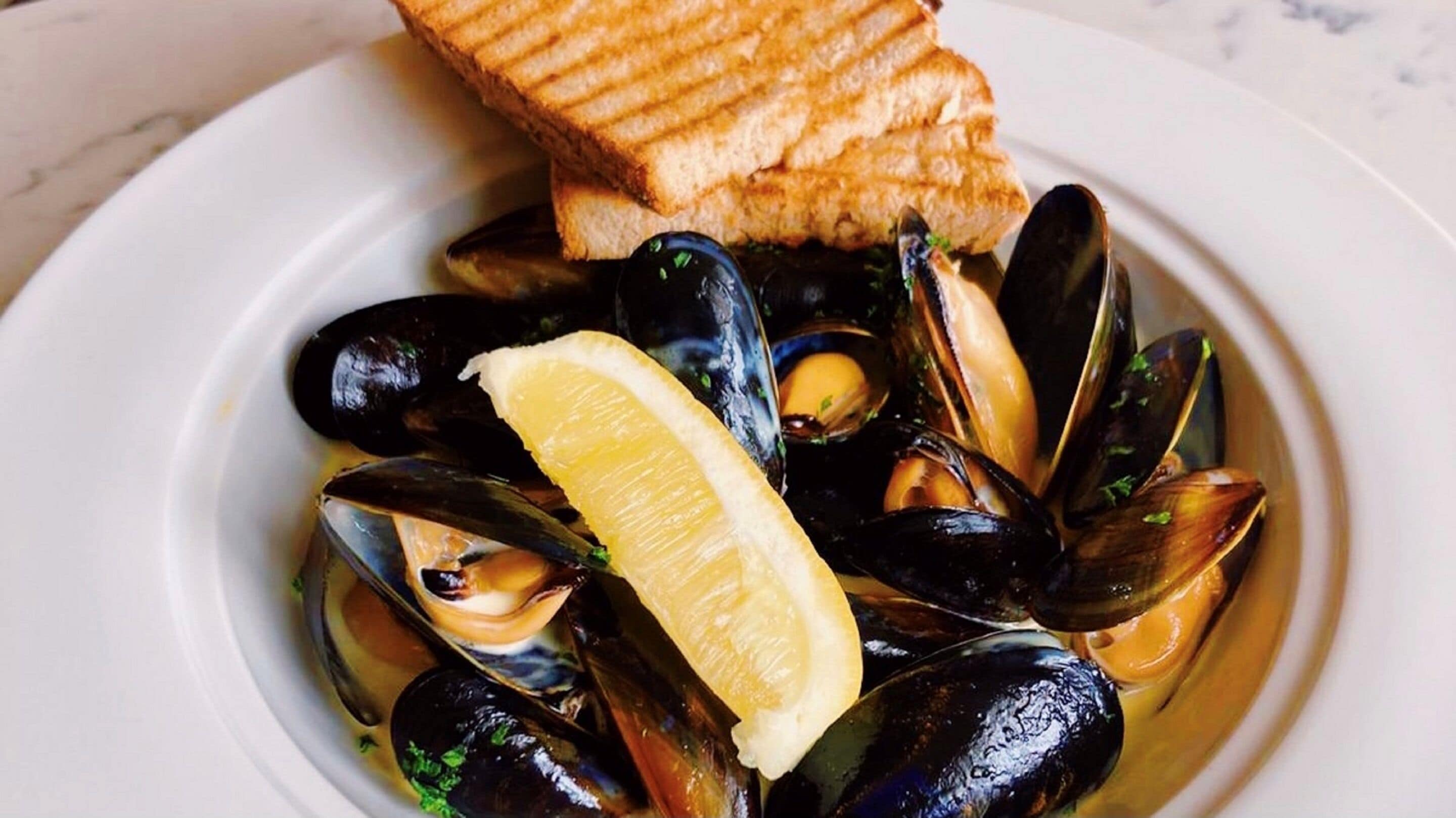 A plate of mussels with a slice of lemon and grilled bread.