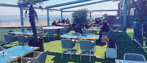 Un espace de restauration en plein air avec des tables et des chaises, un palmier et une vue sur la plage.