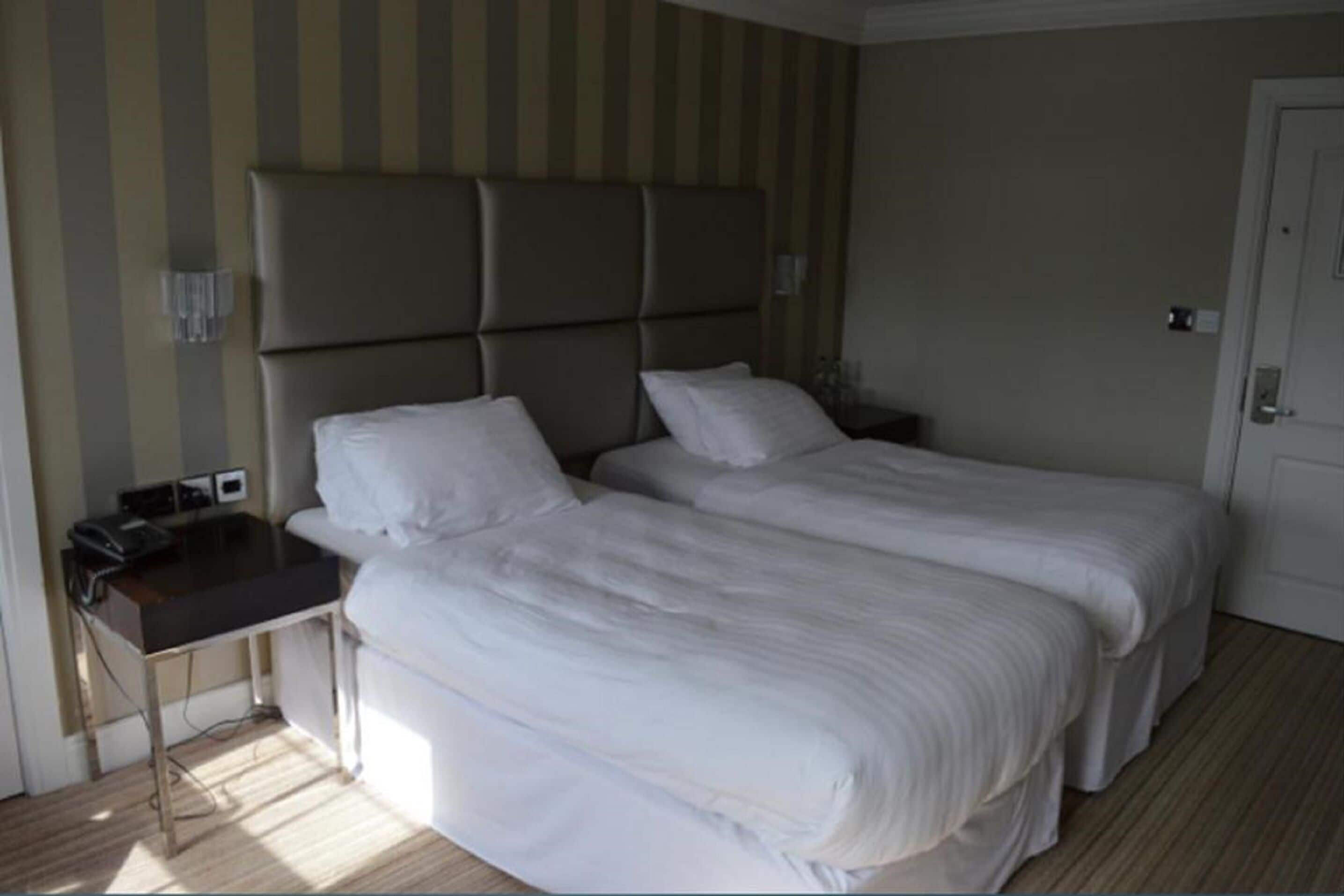 A hotel room with two beds, a bedside table, and a desk with a chair.