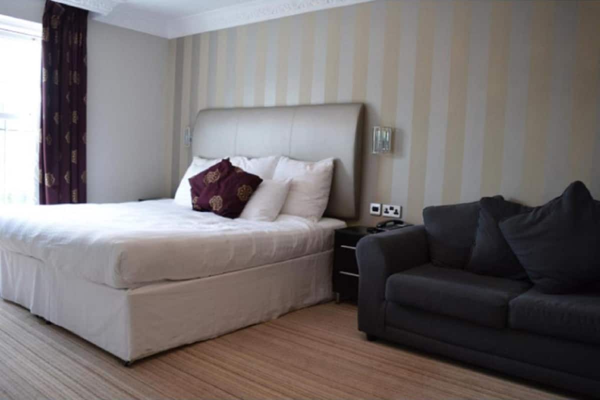 A hotel room with a large bed, a dark sofa, and a striped wall.