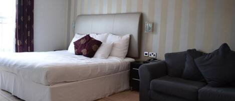 Een hotelkamer met een groot bed, een donkere bank en een gestreepte wand.