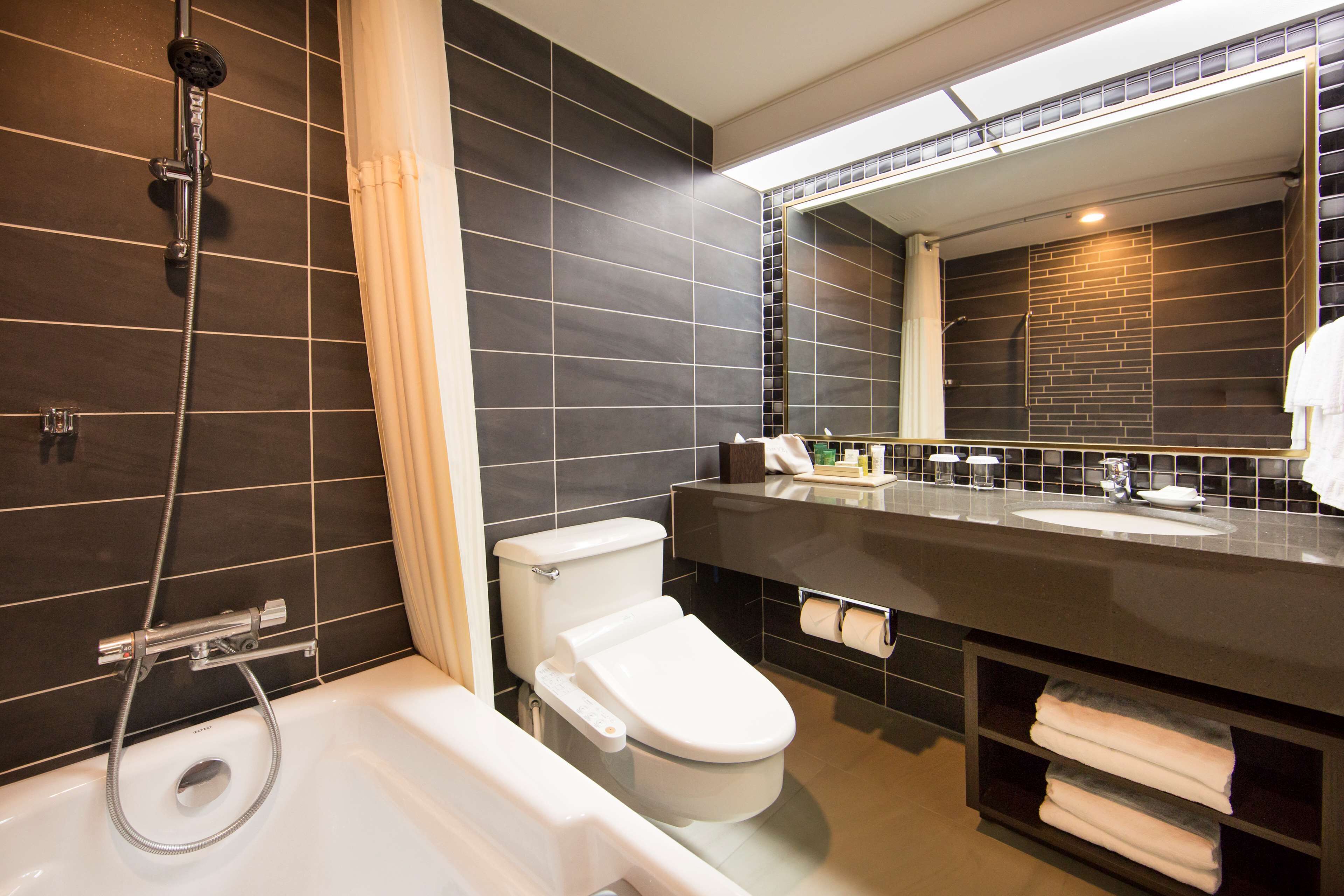A modern bathroom with a bathtub, toilet, and a large mirror above the sink.