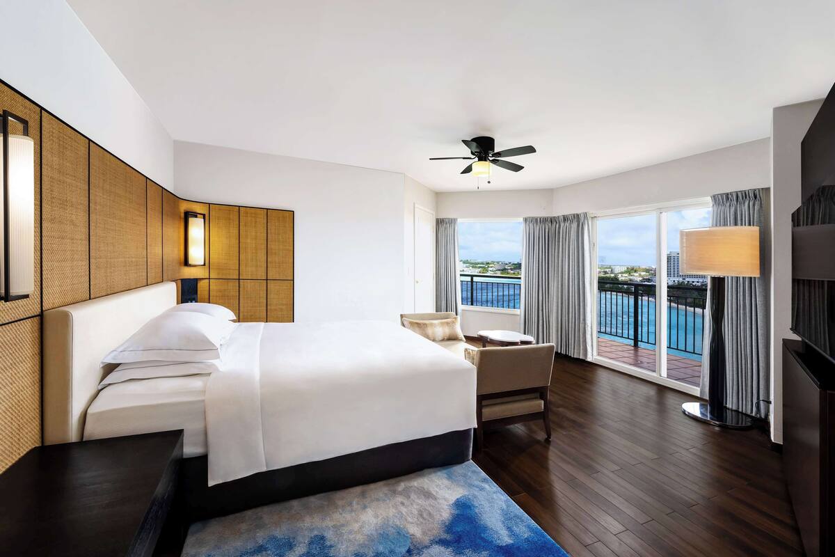Quarto de hotel com uma cama grande, ventoinha no teto, varanda com vista para a piscina e televisão.