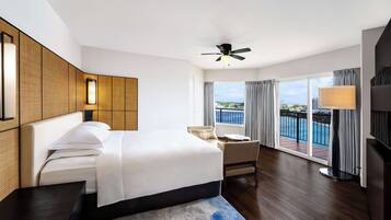 A hotel room with a large bed, a ceiling fan, a balcony with a pool view, and a TV.