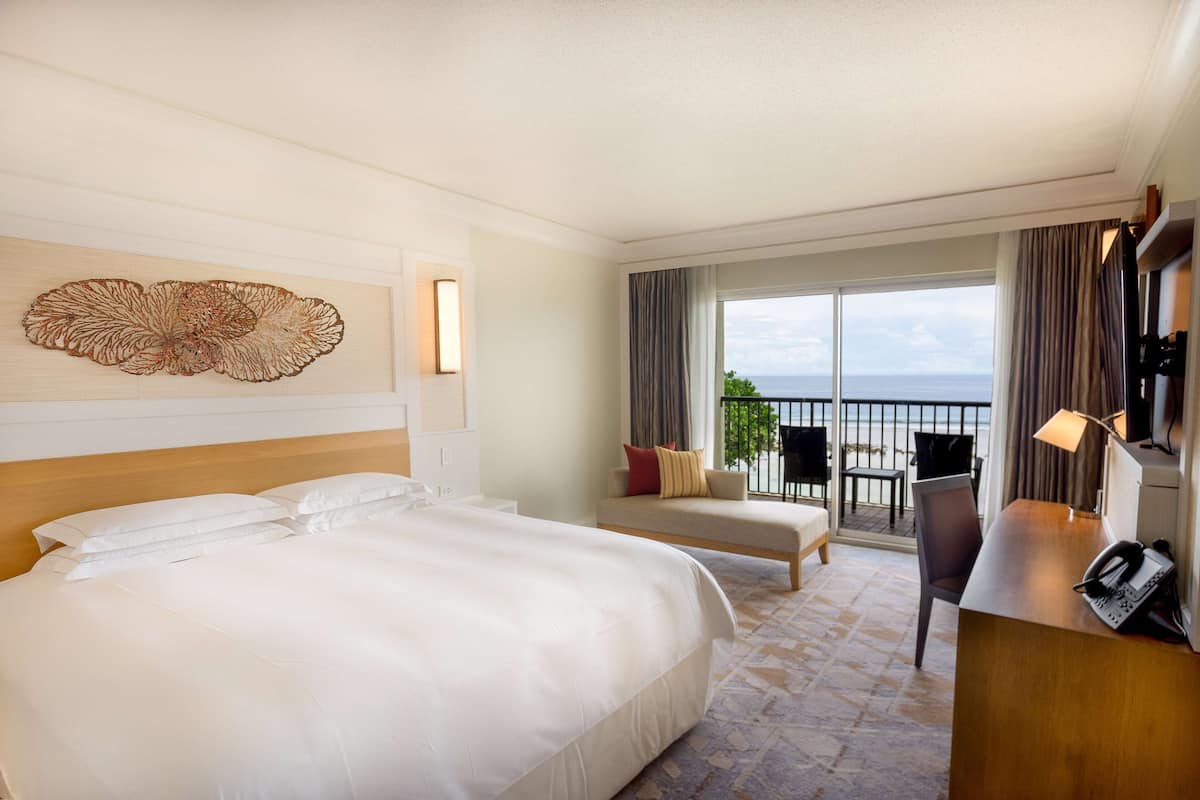 Quarto de hotel com cama grande, secretária com telefone e varanda com vista para o mar.