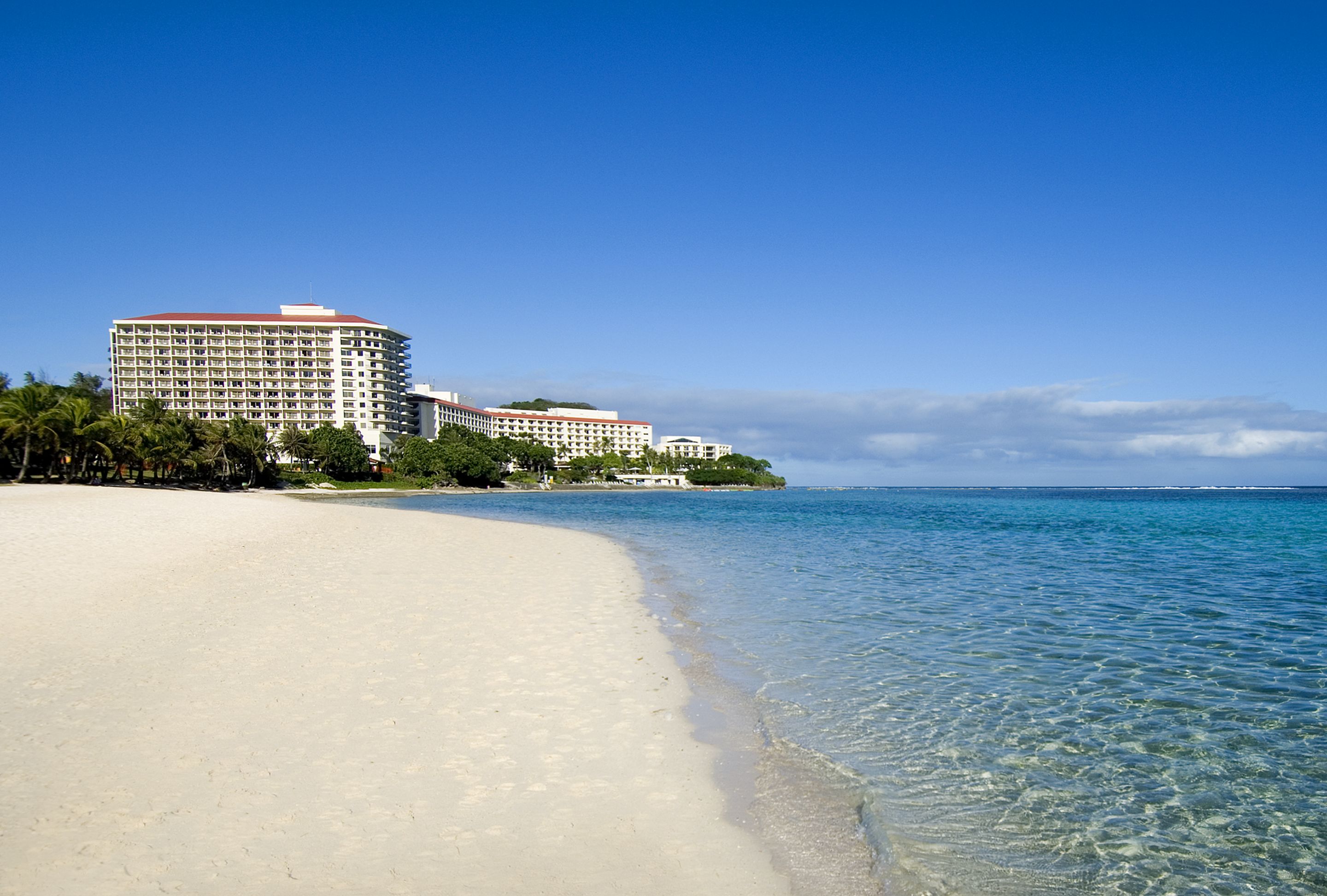 A beachfront hotel with multiple buildings, clear blue water, and a sandy beach.