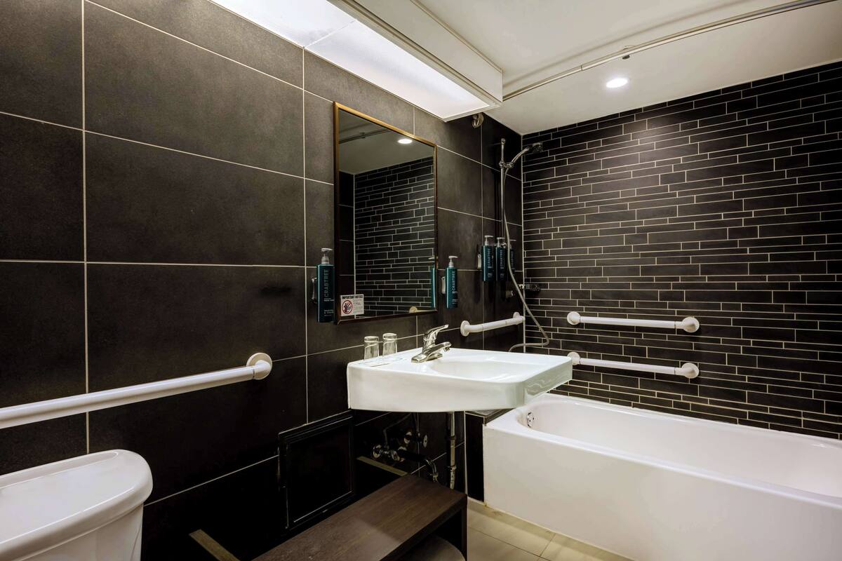 Um banheiro moderno com parede revestida de azulejos pretos, pia branca, banheira e espelho.