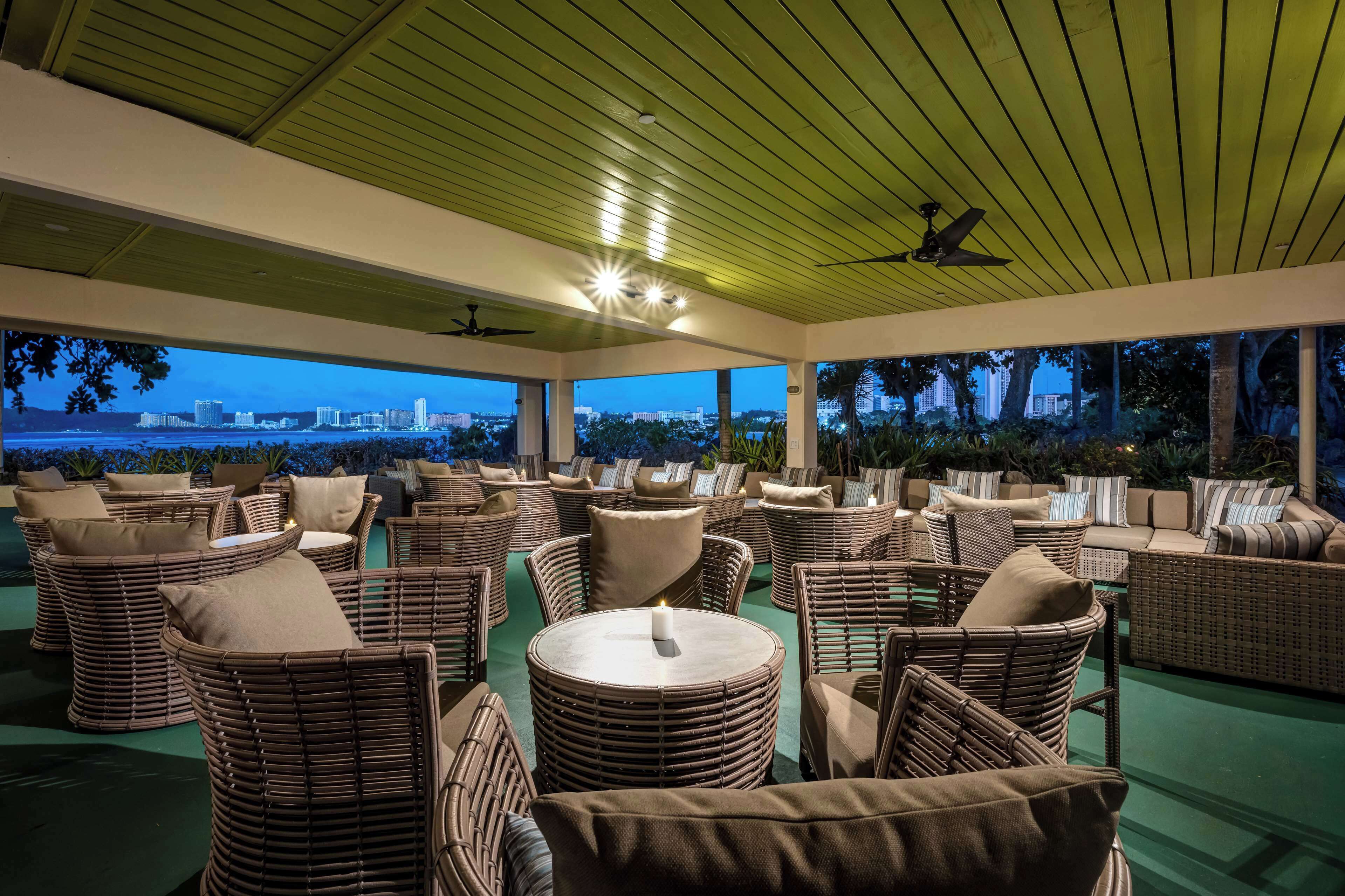 A covered outdoor seating area with wicker furniture and a view of the city skyline at dusk.