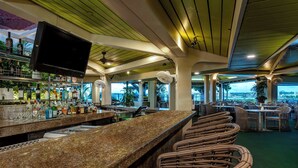 A bar area with a granite countertop, wicker chairs, and a television mounted on the wall. - Hilton Guam Resort And Spa (Tamuning)