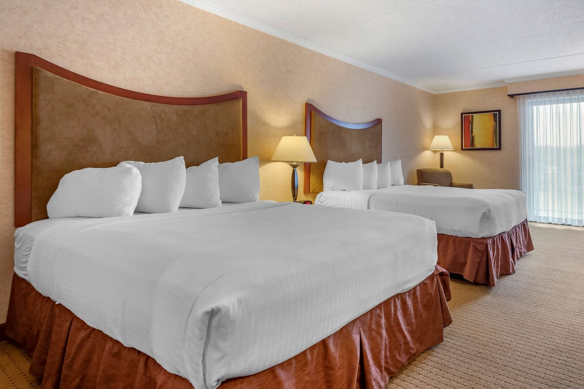 A hotel room with two large beds, a sitting area, and a window with curtains.