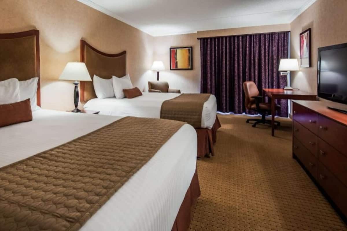 A hotel room with two beds, a desk, a television, and a chair.