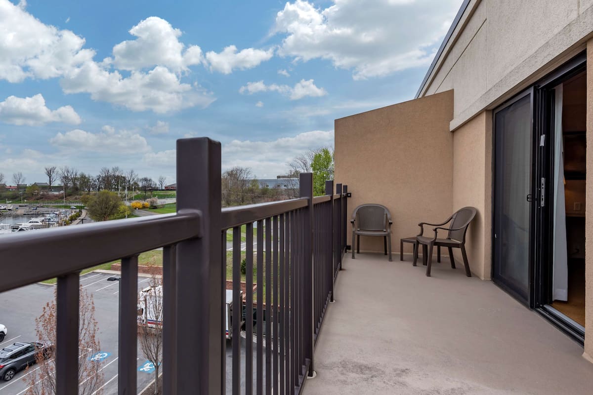 A balcony with a view of a parking lot and a building. There are two chairs and a table on the balcony.