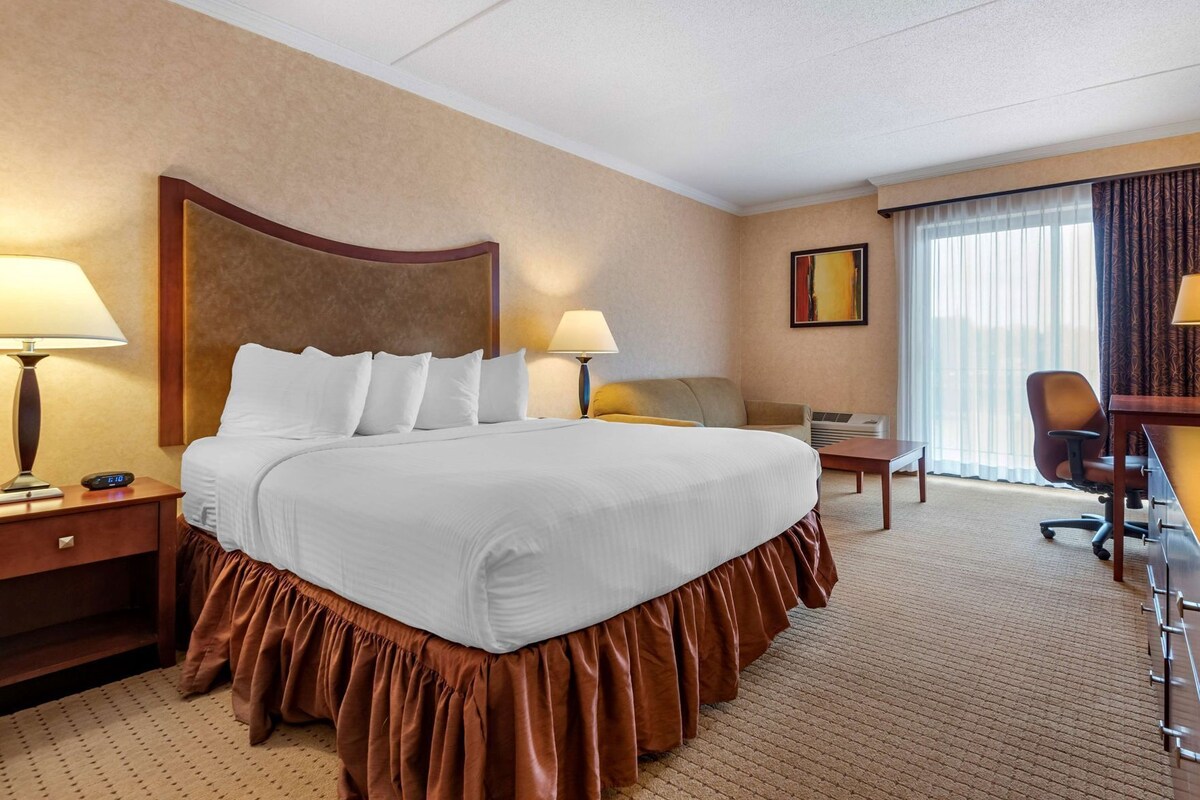 Habitación de hotel con una cama grande, dos mesitas de noche, un escritorio, una silla y un ventanal con cortinas.