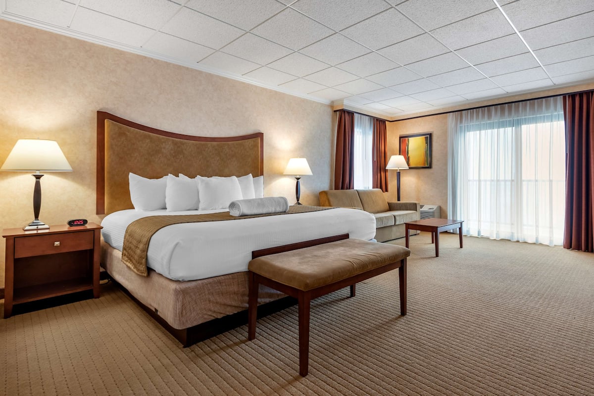 A hotel room with a large bed, two bedside tables, a bench, a sofa, and a window with curtains.