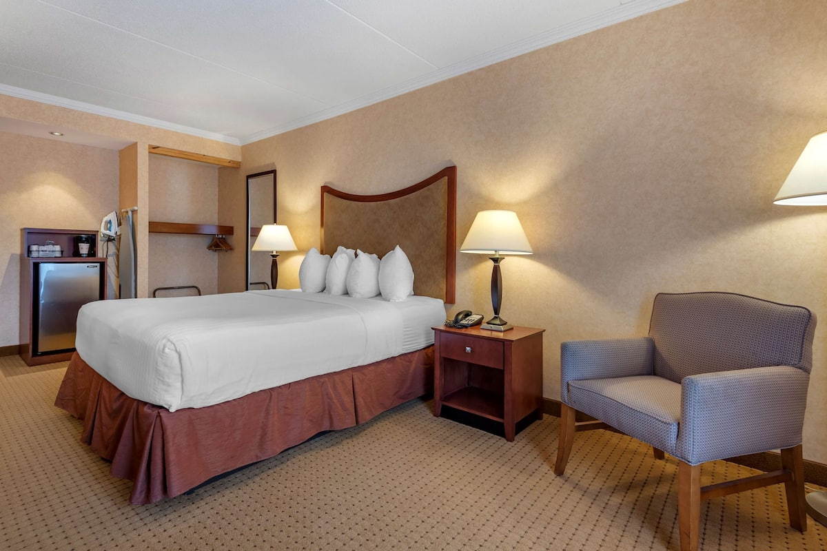 A hotel room with a large bed, a chair, a desk with a lamp, and a minibar.