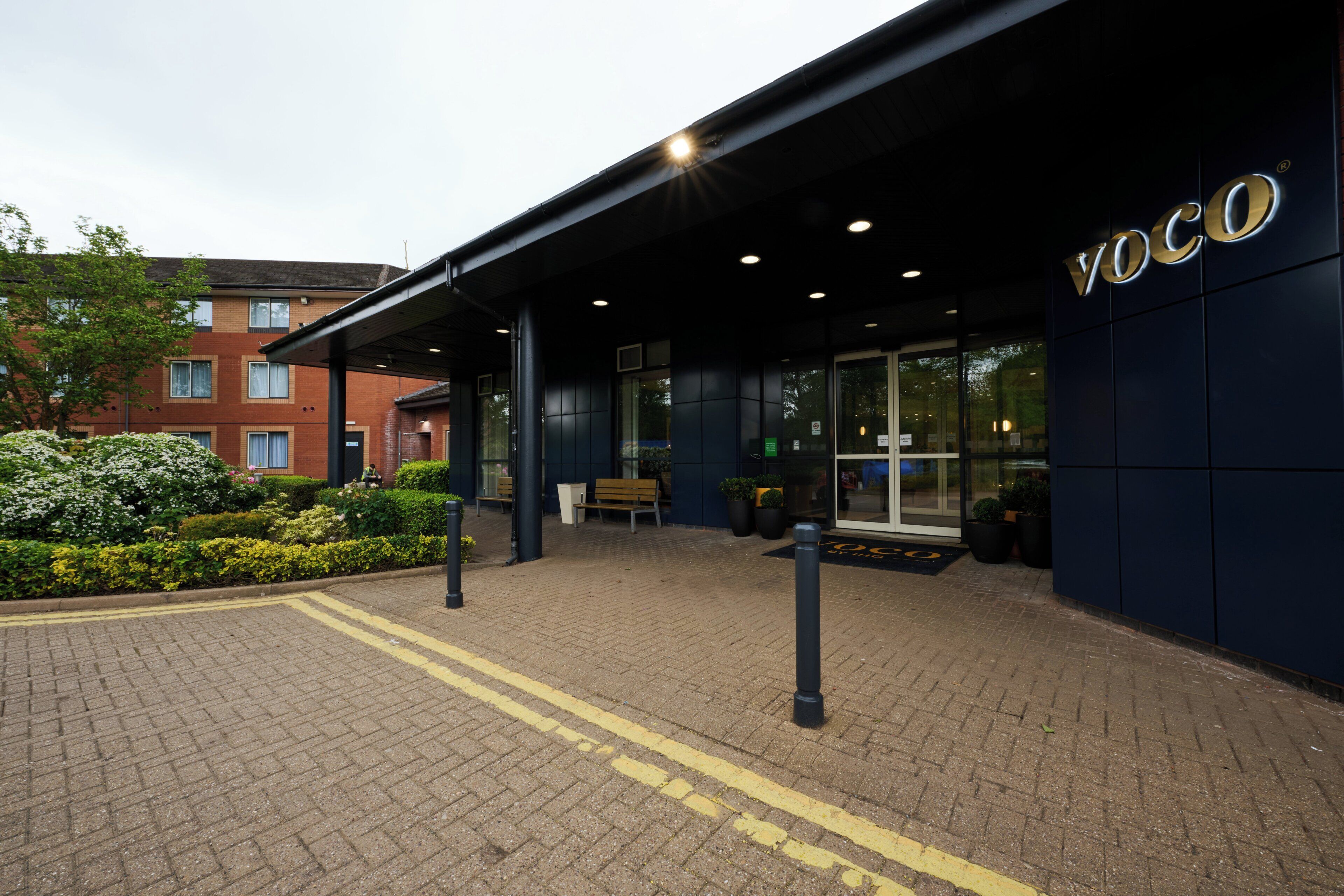 A building with a 'VOCO' sign, a paved entrance, and a bench outside.