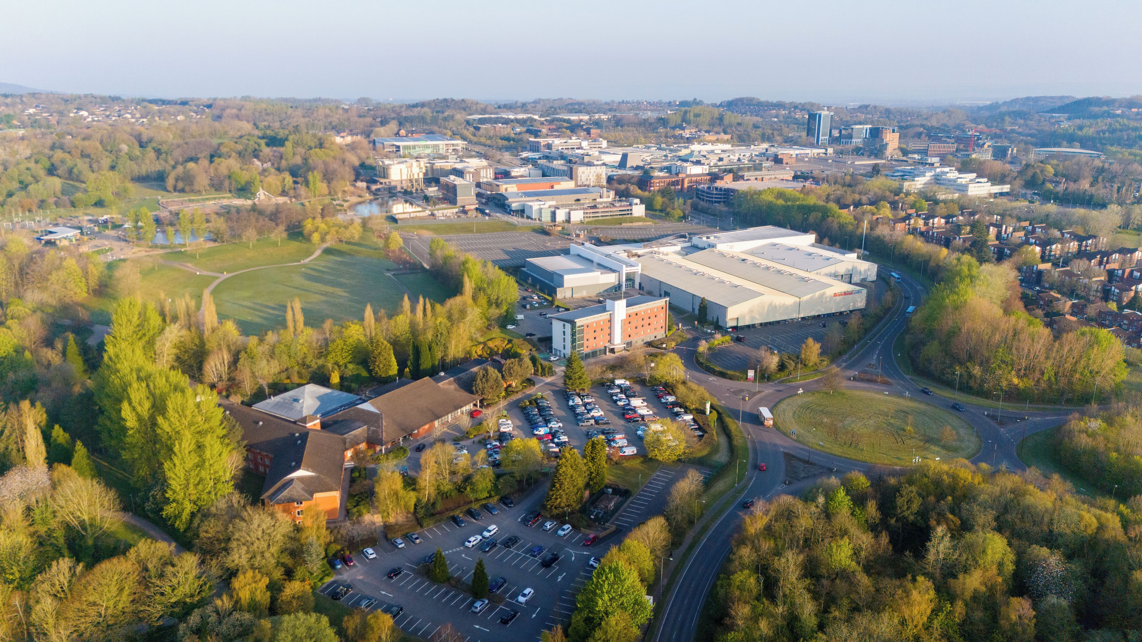 An aerial view of a campus with multiple buildings, parking areas, and surrounding greenery.