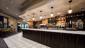 A bar area with a counter, hanging lights, and a variety of bottles and glasses. - voco Telford - Ironbridge by IHG (Telford)