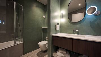 Un baño moderno con ducha envuelta en vidrio, inodoro, tocador con espejo e iluminación integrada.