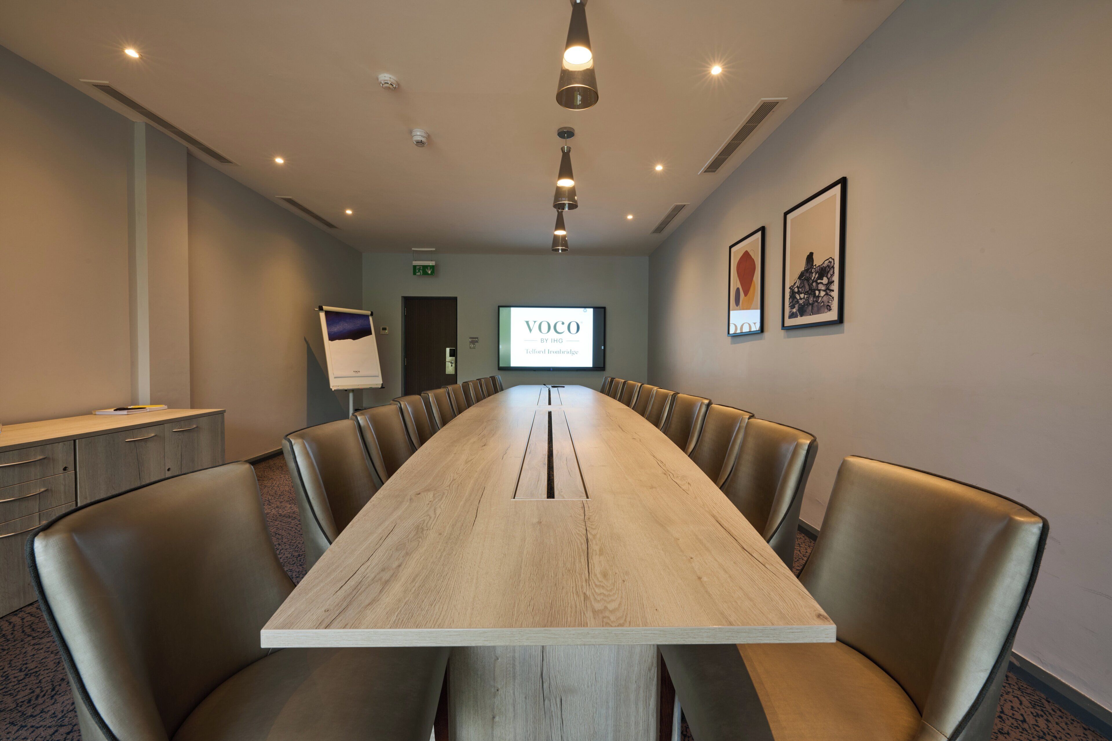 A conference room with a long table, leather chairs, a screen displaying 'VOCO BY ING,' and framed artwork on the wall.