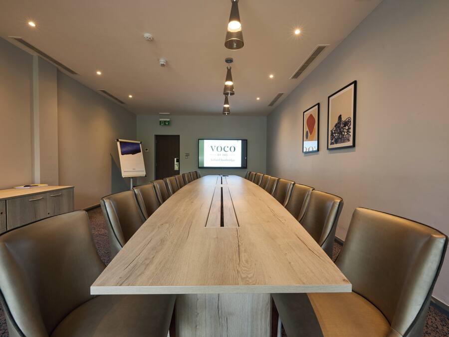 A conference room with a long table, leather chairs, a screen displaying 'VOCO BY ING,' and framed artwork on the wall.