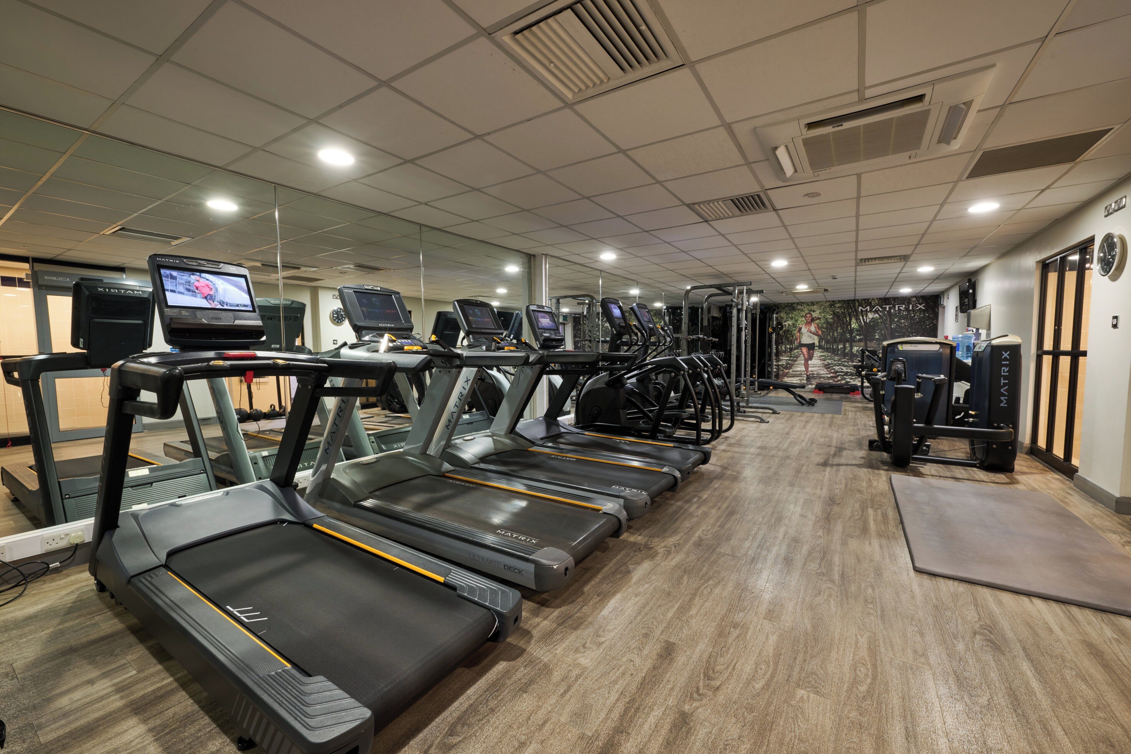 Een fitnessruimte met loopbanden, trainingsapparatuur en een spiegelwand.