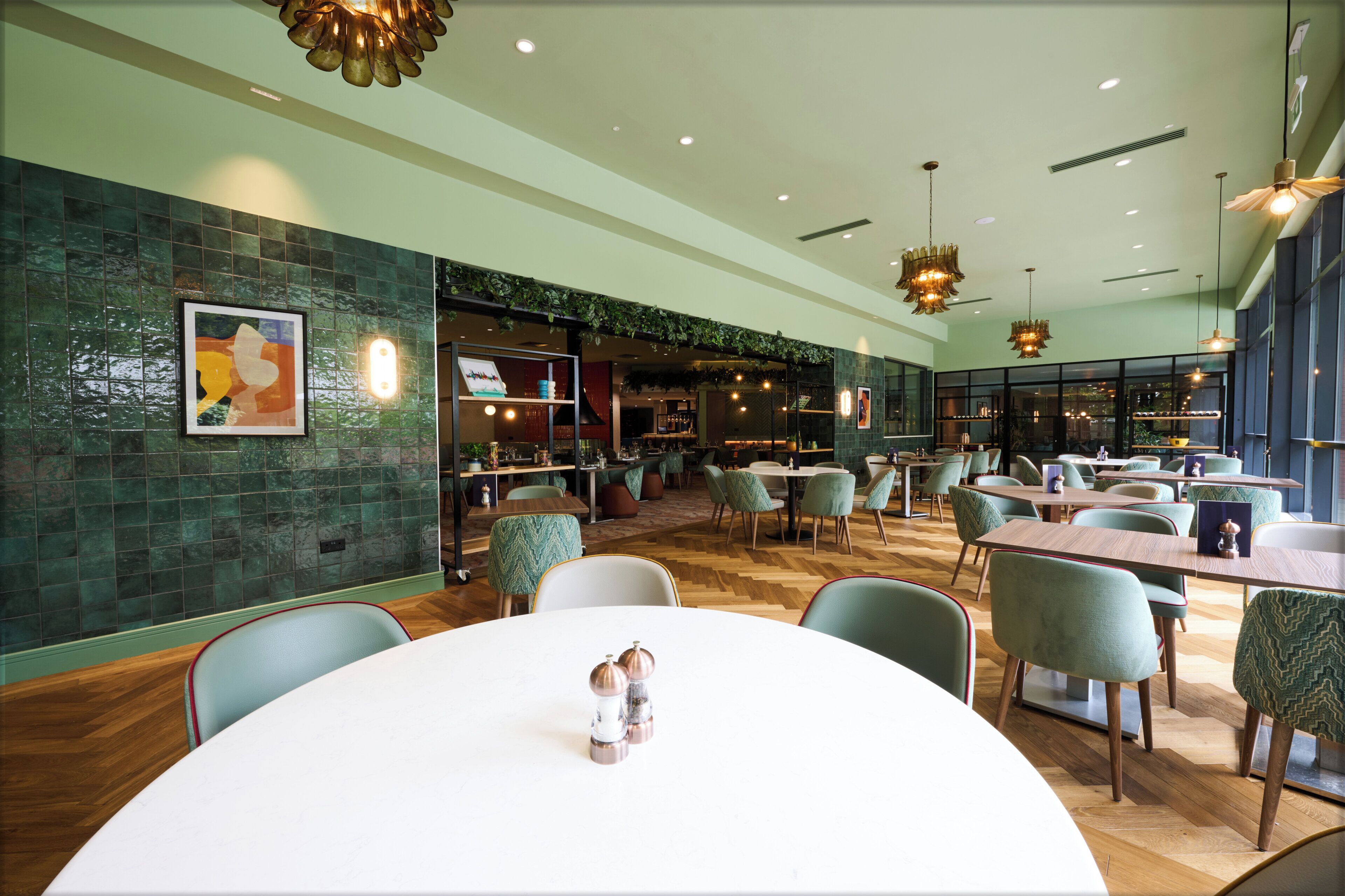 Un restaurante con mesas redondas, sillas y una pared de azulejos verdes.