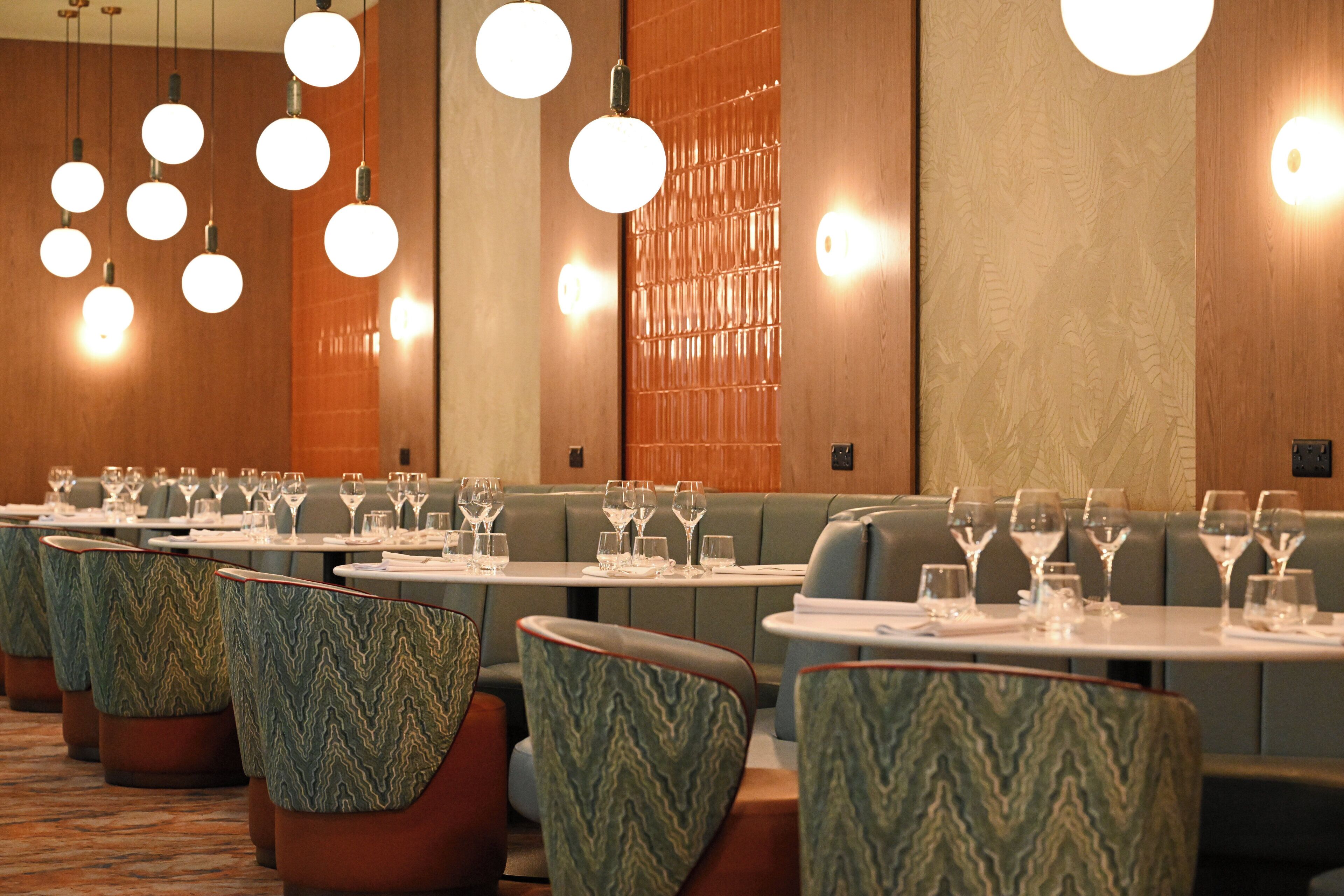 Ein Restaurant mit mehreren Tischen und Sitzecken, an jedem Tisch Geschirr und Besteck.