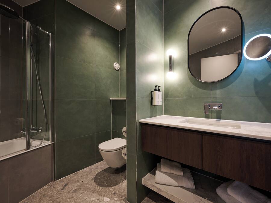 Un baño moderno con ducha de vidrio, inodoro, tocador con espejo y lavamanos.