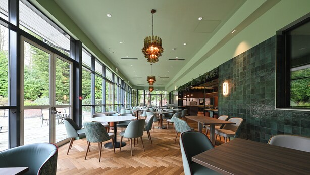 A spacious indoor area with large windows, wooden flooring, and multiple seating arrangements. - voco Telford - Ironbridge by IHG (Telford)