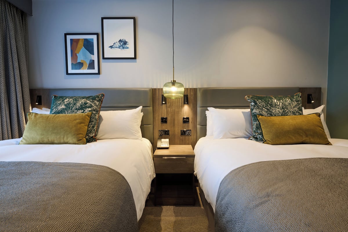 A hotel room with two beds, a nightstand, a telephone, and wall-mounted lights.