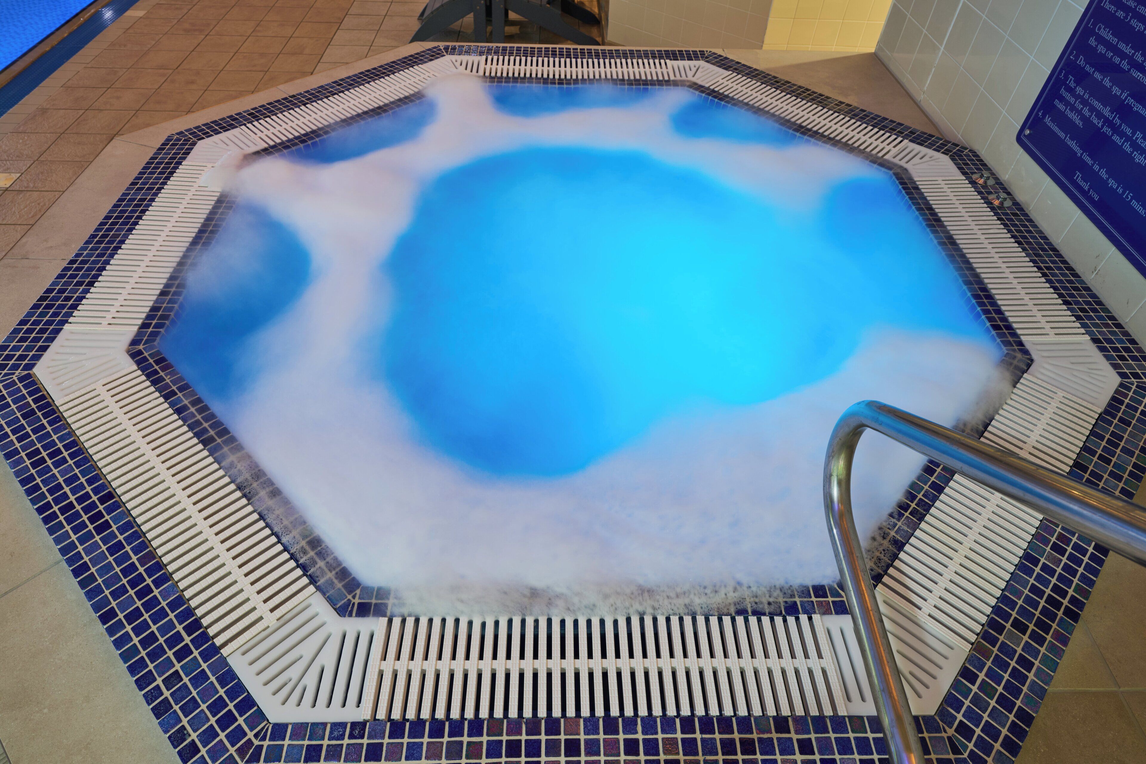 Un bain à remous avec un bord carrelé et une échelle en métal.
