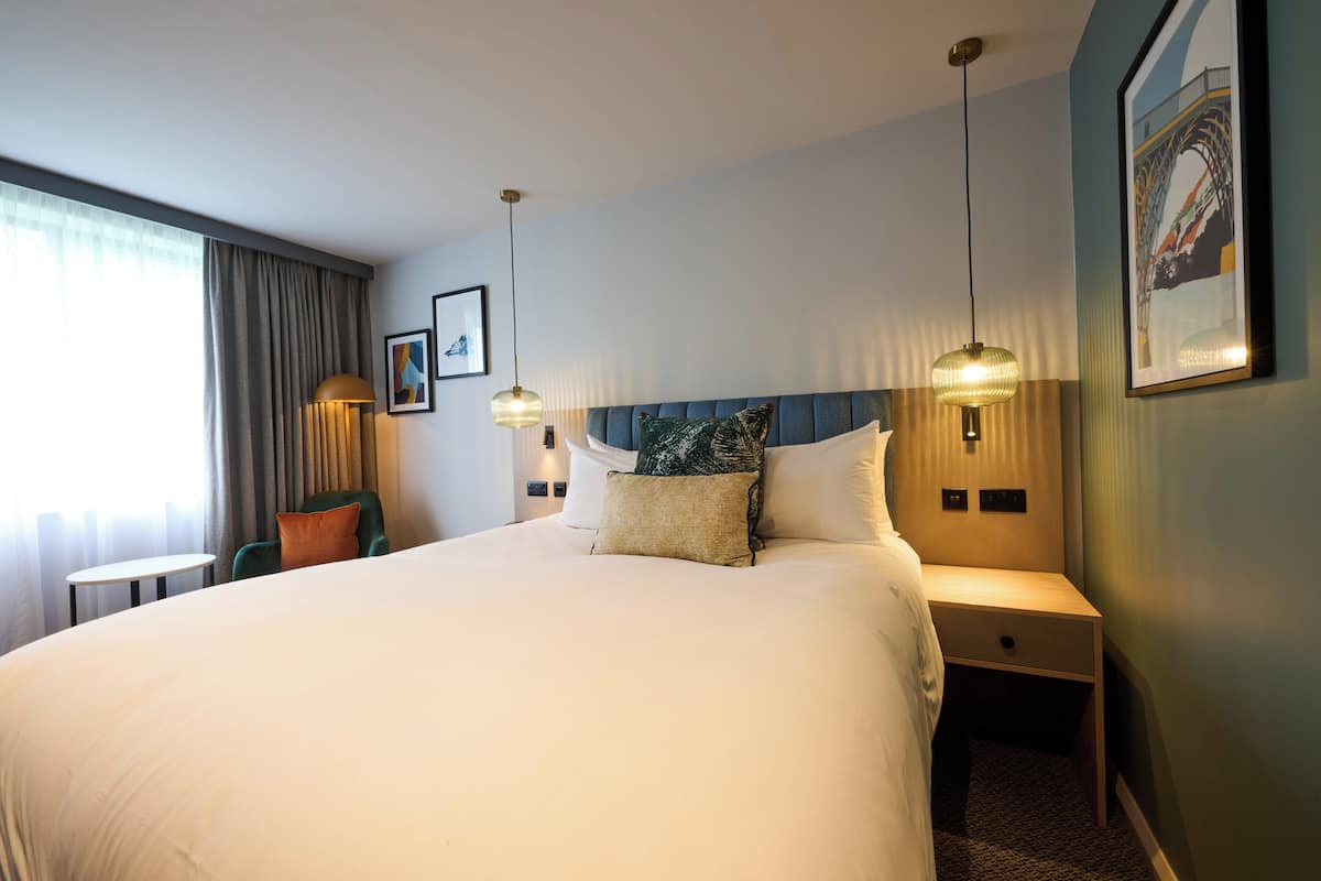 A hotel room with a large bed, bedside tables, a chair, and a view of the outdoors.