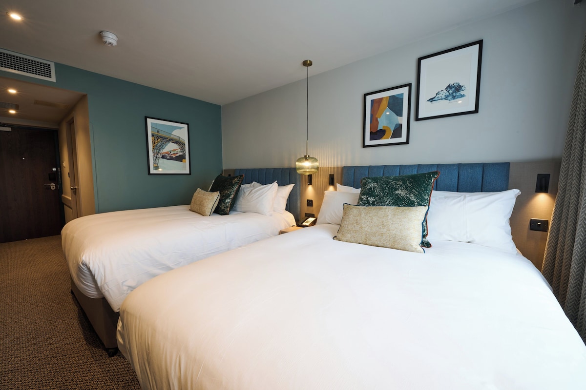 A hotel room with two beds, a blue accent wall, and framed artwork.