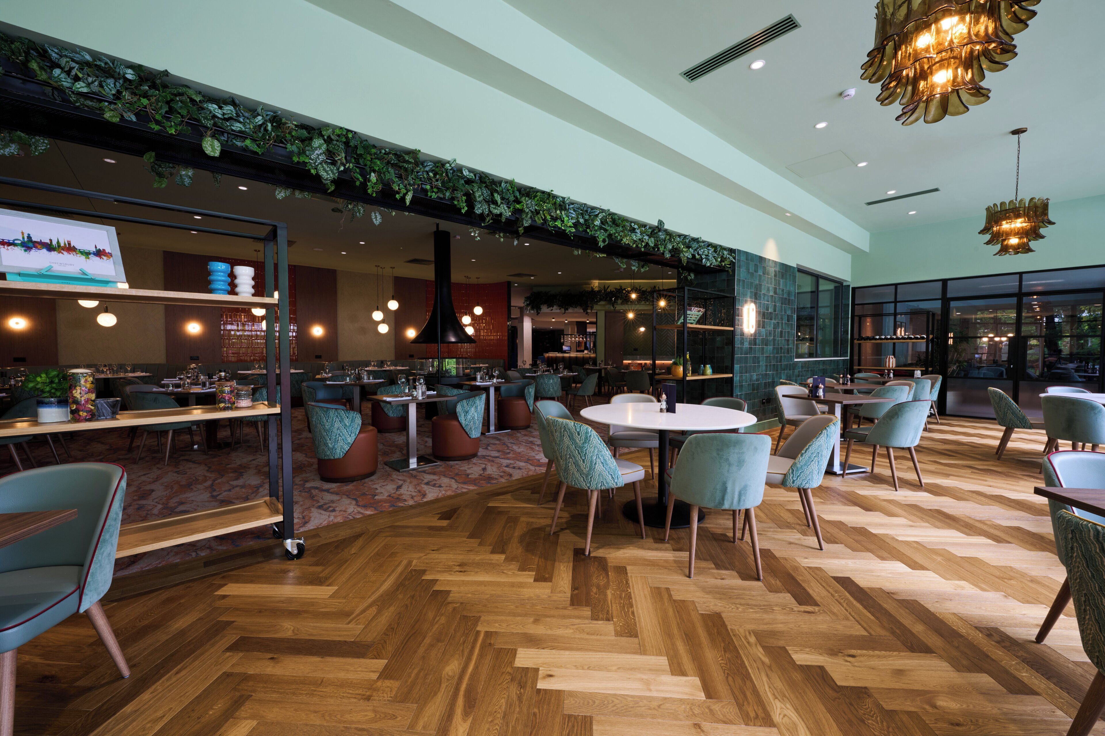 Un ristorante moderno con pavimento a spina di pesce, tavoli rotondi e sedie color petrolio.