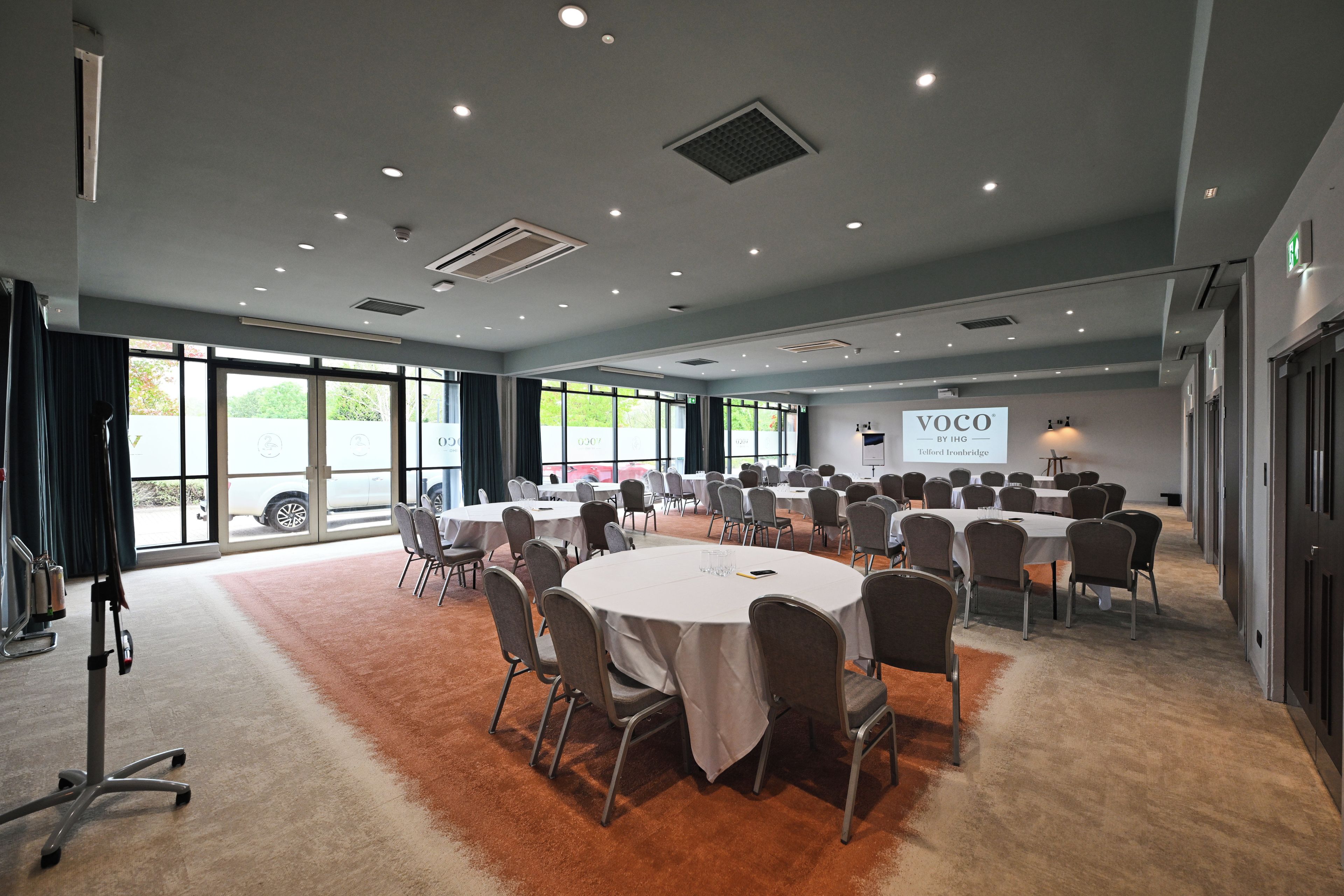 A conference room with round tables and chairs, large windows, and a projector screen.