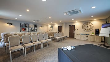 Una sala de conferencias con filas de sillas, una mesa con una computadora portátil, un reloj y una pantalla de proyector.