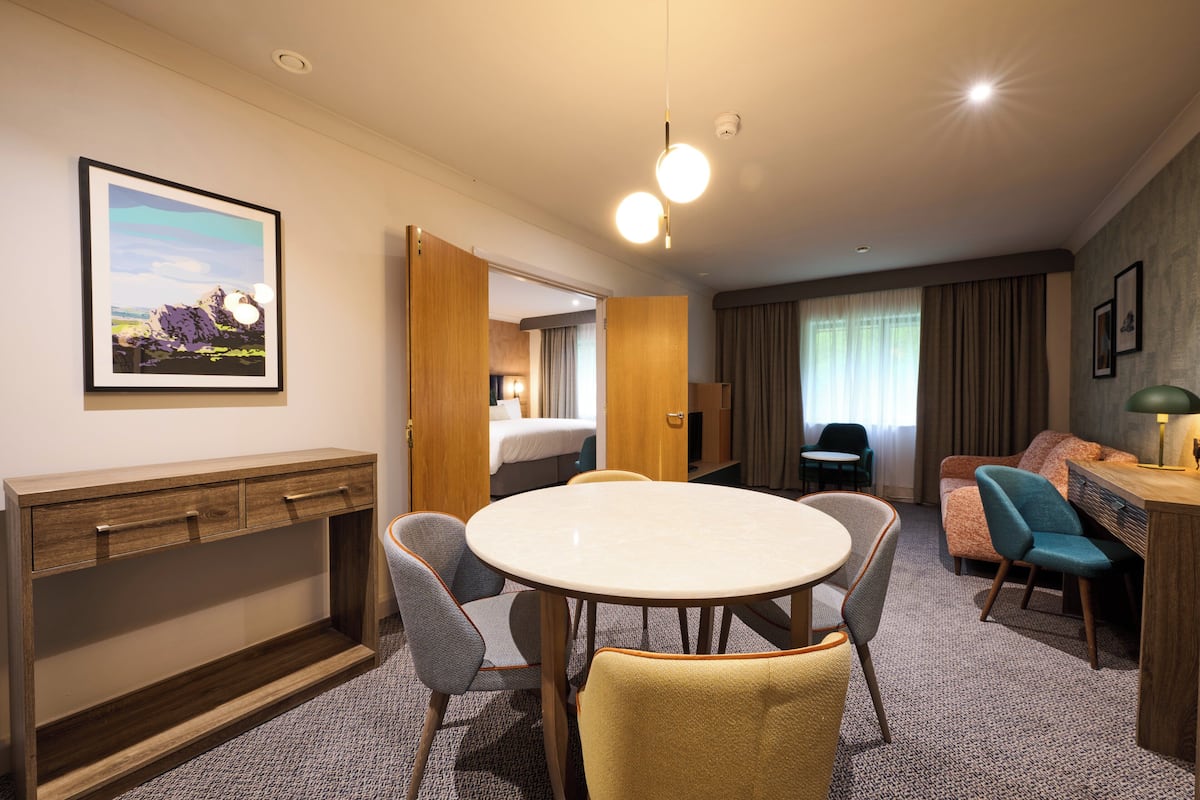 A hotel room with a bed, a desk, a round table with chairs, a sofa, and a picture on the wall.
