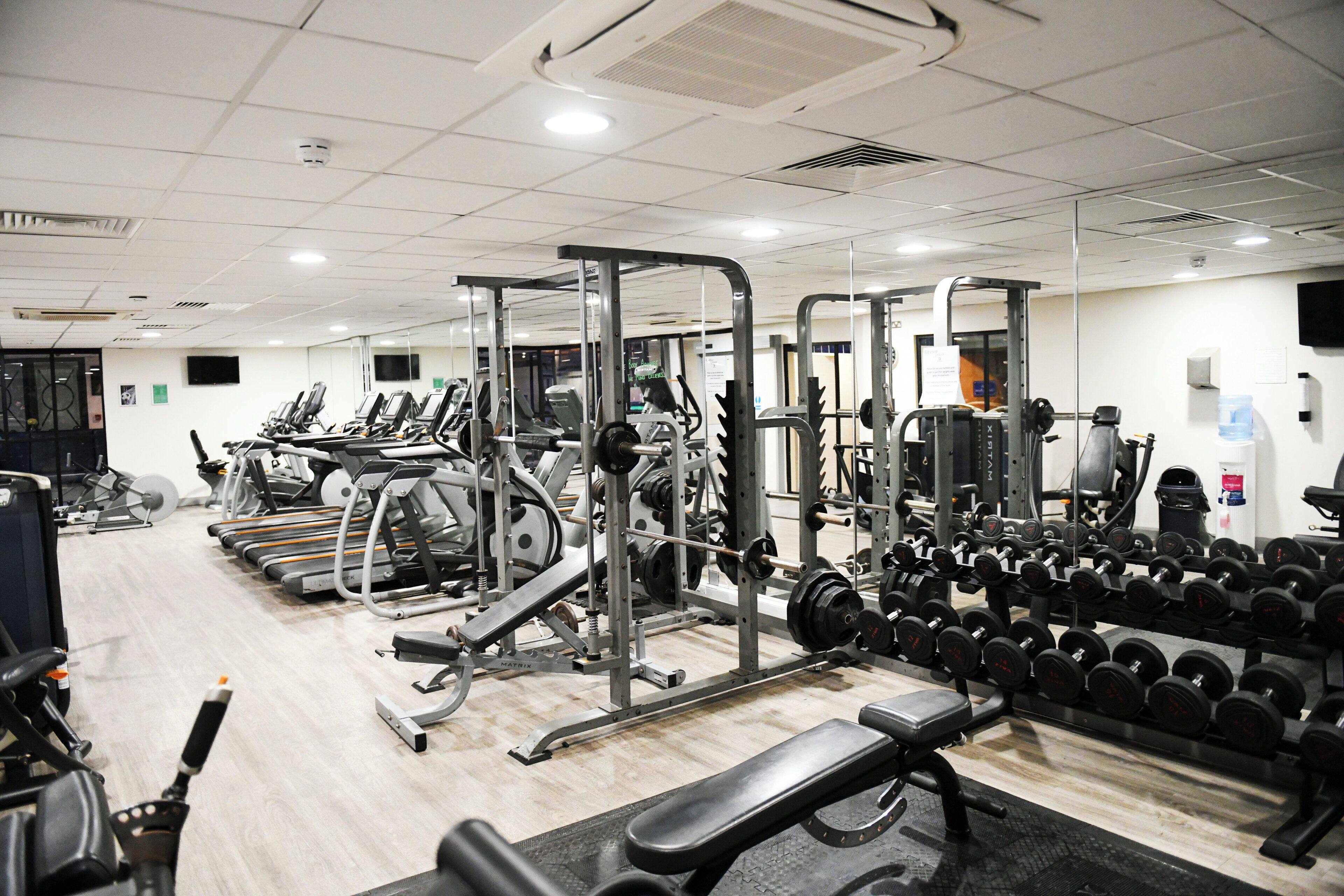 A gym with various exercise equipment, including treadmills, weight machines, and dumbbells.